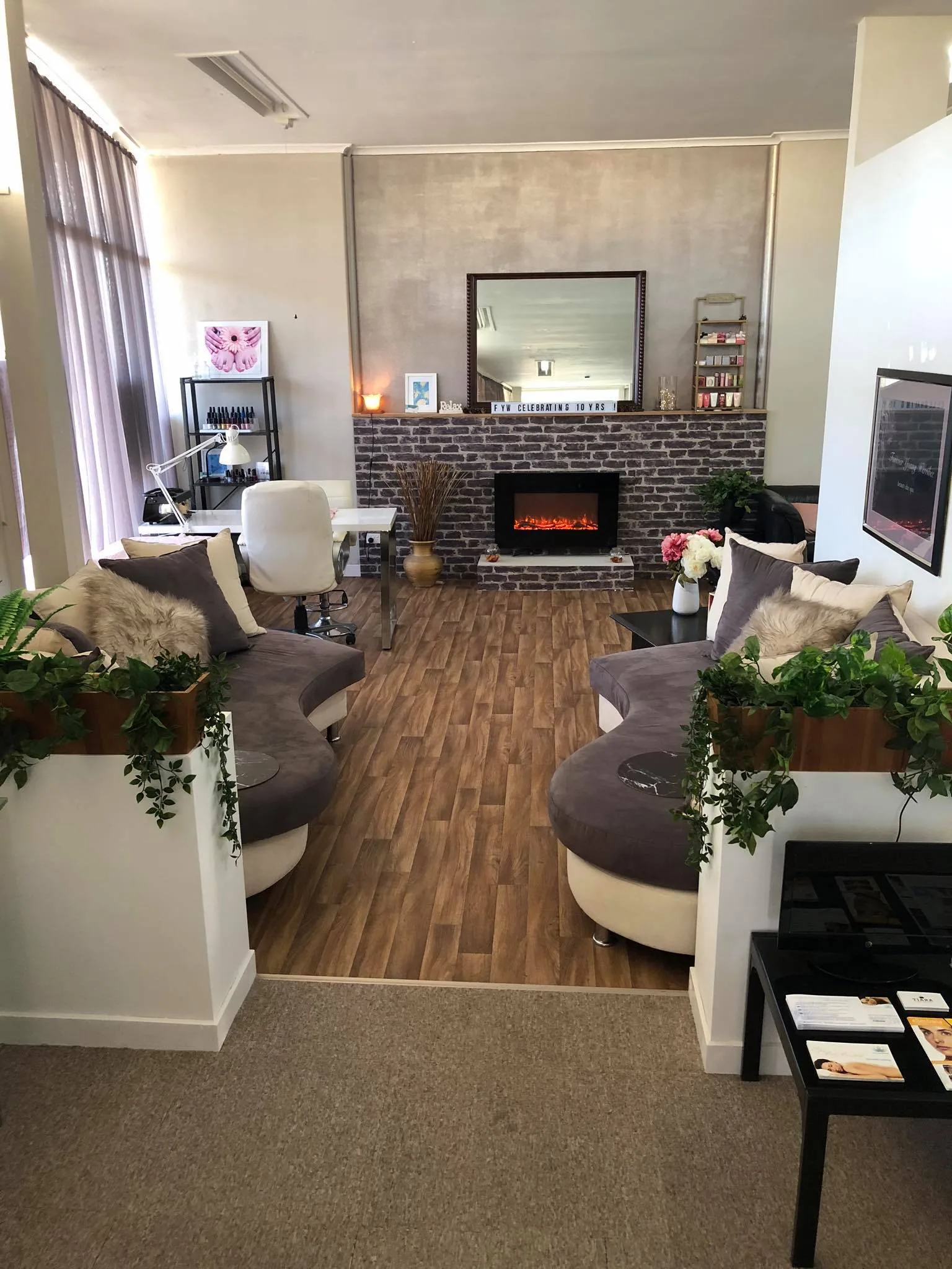 Forever Young Werribee salon lounge with curved velvet sofas, brick electric fireplace and a letterboard reading 'FYW CELEBRATING 10 YRS'